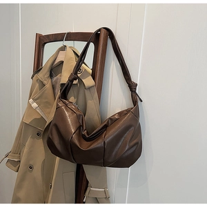 Detail of a brown pleated crescent bag with a knotted strap on a wooden rack