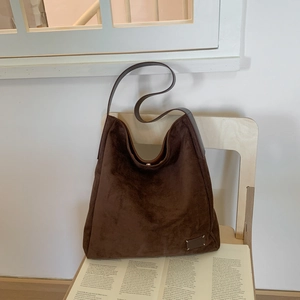 Close-up of dark brown suede hobo bag with signature four-stitch detail on a wooden chair