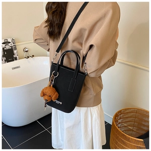 Detail of black leather mini tote bag with crossbody strap and cute dog charm pendant