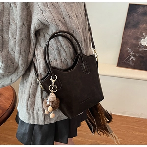 Detail of dark brown matte bucket bag with plush charm and embossed fashion text