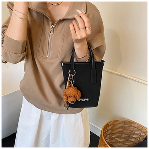 Detail of a minimalist black leather bucket bag with a cute brown plush poodle charm