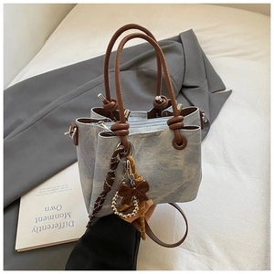 Close-up of light blue denim bucket bag with brown bow detail and metal beads