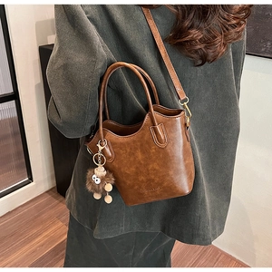 Close-up of vintage brown leather bucket bag featuring fashion text and cute plush monster charm