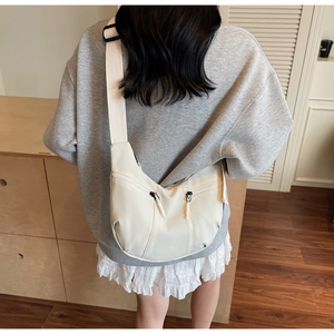Gros plan d'un sac demi-lune blanc cassé avec bandoulière réglable porté par un mannequin