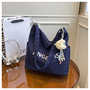Detail of navy blue nylon tote bag with white lettering and yellow moon plush charm