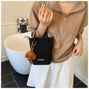 Detail of black mini tote bag with silver CINO'2AD logo and brown teddy dog charm