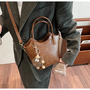 Detail of brown litchi pattern leather bucket bag with cute plush pendant and wave opening