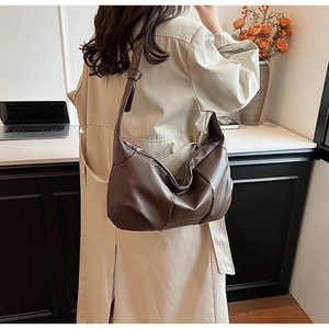 Deep brown soft leather shoulder bag with pleated design worn by a model in a beige coat