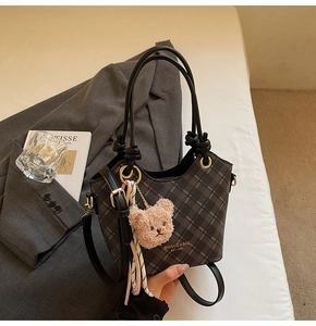 Dettaglio di una borsa a secchiello a quadri grigi con manici in pelle annodati e ciondolo