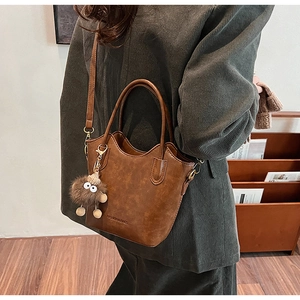 Brown tote bag detail with textured finish and cute plush monster charm accessory