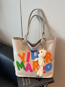 Light gray canvas tote bag with colorful letters and a cute plush bear charm accessory