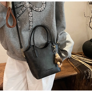 Detail of black tote bag featuring scalloped edges, ring handles and furry pom-pom charm