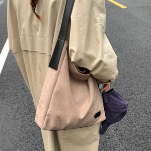 Close-up of light brown suede tote bag with black strap worn over a trench coat