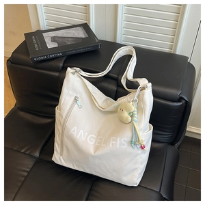 Close-up of white canvas tote bag with black Angel Fish text and moon plush pendant