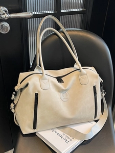 Beige large capacity travel duffel bag in matte leather on a black leather chair