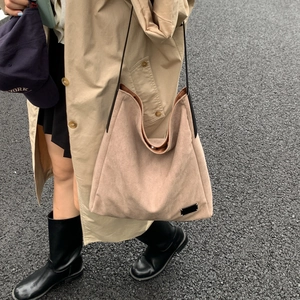 Detail of khaki suede hobo tote bag worn with a beige trench coat in an outdoor setting