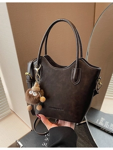 Dark brown leather bucket tote bag with plush monster charm on minimalist background