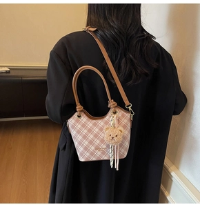 Dettaglio borsa a secchiello a quadri rosa con tracolla in pelle marrone e ciondolo a orsetto