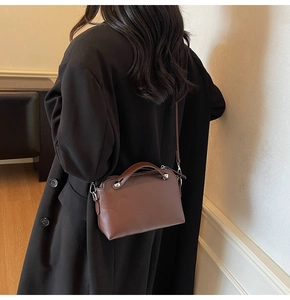 Detail einer braunen Lederhandtasche mit breitem Griff und Nieten auf schwarzem Mantel
