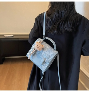 Detailed view of light blue lace crossbody bag with ribbon and small bear charm detail