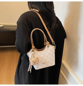 Dettaglio di una borsa a secchiello a scacchi beige con tracolla in pelle e ciondolo orso