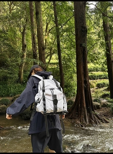 Foto exterior de una mochila funcional gris claro con correas ajustables en el bosque
