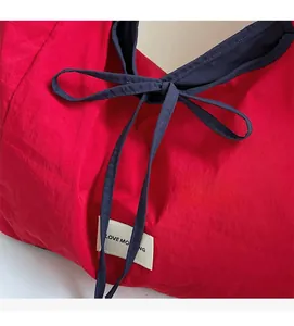 Detail of red nylon tote bag with navy blue bow tie and LOVE MORNING woven label