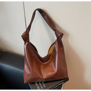 Detail of dark brown leather tote bag showing handcrafted knot accents on the shoulder strap