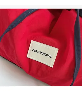 Detail of red nylon tote bag featuring white Love Morning label and blue fabric strap