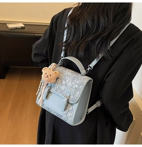 Light blue bow-knot backpack with plush bear charm shown on model in a soft indoor setting