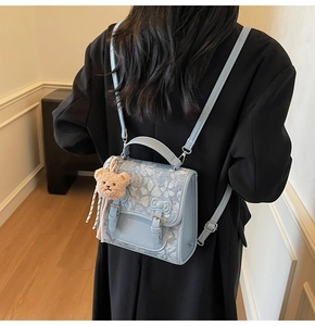 Detail view of a light blue floral backpack with buckle straps and a plush bear pendant