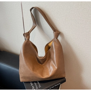 Detail of a brown PU leather tote bag with a knotted strap on an artistic book background