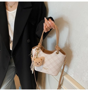 Dettaglio borsa a secchiello beige a quadretti con manici in pelle e ciondolo orsetto