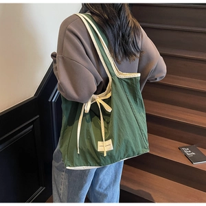 Detail of dark green canvas tote bag with cream trim and side bow on dark wood stairs