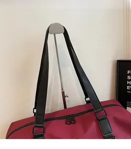 Detail of reinforced shoulder strap and dual metal zippers on a burgundy travel duffel bag