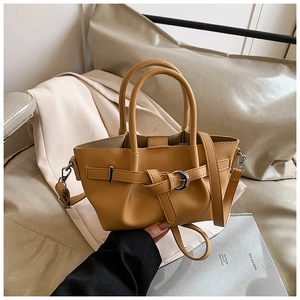 Détail du sac à main en cuir caramel avec boucle argentée et poignées rondes en lumière douce