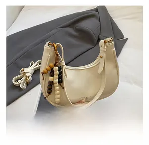 Detail view of cream hobo bag with wood bead charm and adjustable shoulder strap
