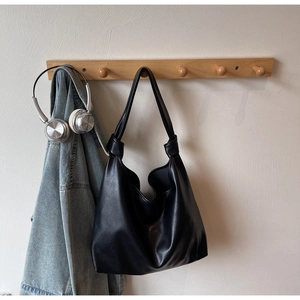 Detail of black leather hobo tote bag with knot strap hanging on a wooden hook