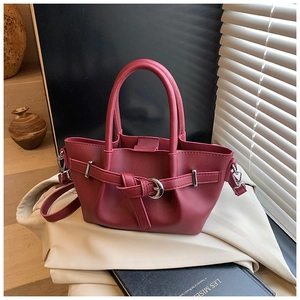 Détail du sac seau plissé bordeaux avec boucle métallique et poignée sous une lumière chaude