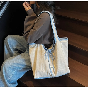 Lifestyle shot of woman carrying cream and light blue tote bag with ribbon detail