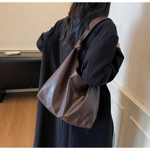 Detail of dark brown soft leather tote bag with knot strap on a shoulder model