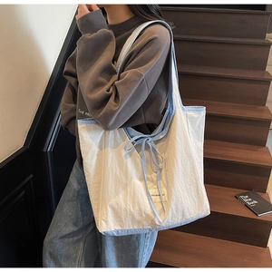 Close-up of a white tote bag with light blue straps and a bow detail in a lifestyle setting