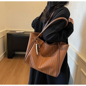 Detail of a brown woven tote bag featuring stylish wood bead charms and slim shoulder straps