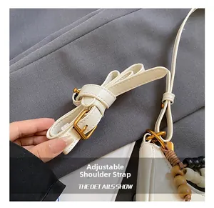 Detail of adjustable strap on white leather bag with gold buckle and beaded charm