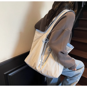 Detail of canvas tote bag with light blue straps and side drawstring on model
