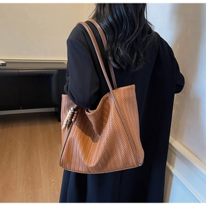 Detailed texture of brown woven tote bag with beaded pendant shown on model