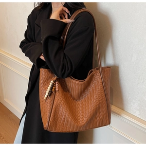 Detail einer braunen Web-Tote-Bag mit Chevron-Muster und modischem Perlenanhänger am Riemen