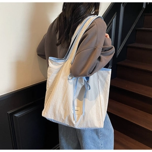 Detail view of cream nylon tote bag featuring blue ribbon bow and decorative woven label