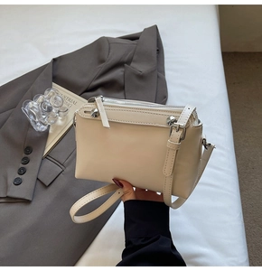 Detailansicht einer cremefarbenen Handtasche mit Silber-Reißverschlüssen und Nieten