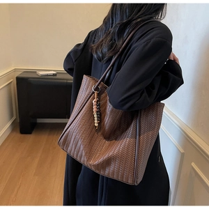 Detailed V-pattern woven brown tote bag with leather trim and ethnic beaded pendant charm